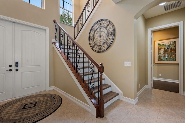 stairs with arched walkways, a high ceiling, visible vents, baseboards, and tile patterned floors