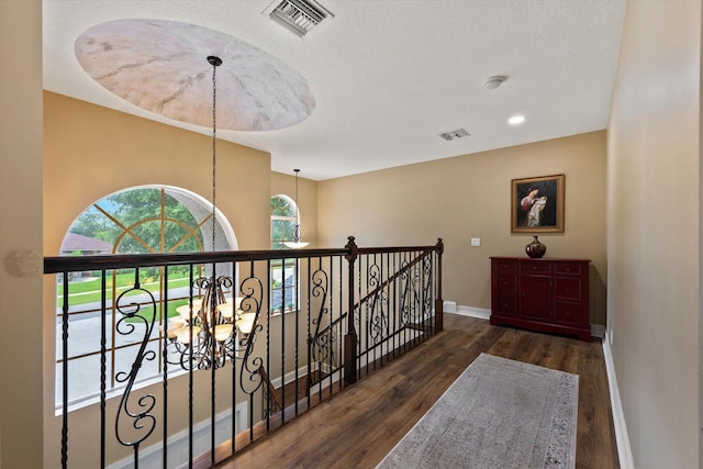 hallway with baseboards, visible vents, wood finished floors, and an upstairs landing