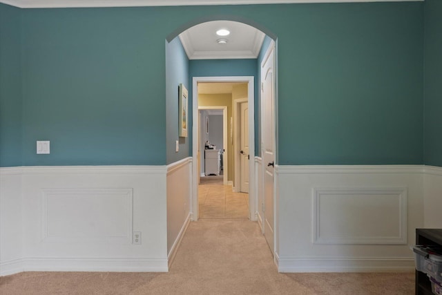 hallway with arched walkways, ornamental molding, and light colored carpet