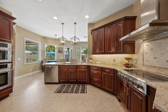 kitchen featuring appliances with stainless steel finishes, a peninsula, hanging light fixtures, wall chimney range hood, and backsplash