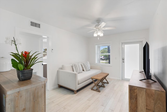 living area featuring visible vents, baseboards, ceiling fan, and light wood finished floors