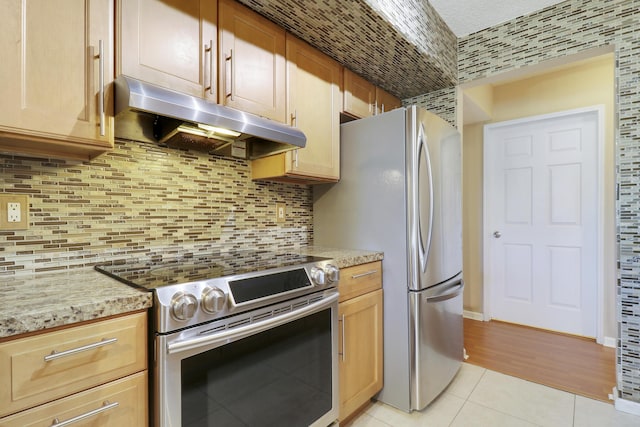 kitchen featuring decorative backsplash, appliances with stainless steel finishes, light tile patterned flooring, light stone countertops, and under cabinet range hood