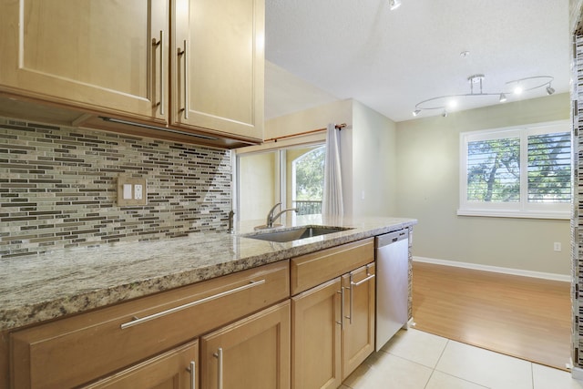 kitchen featuring light tile patterned floors, light stone counters, a sink, dishwasher, and tasteful backsplash