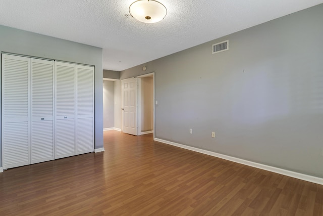 unfurnished bedroom featuring baseboards, a textured ceiling, visible vents, and wood finished floors