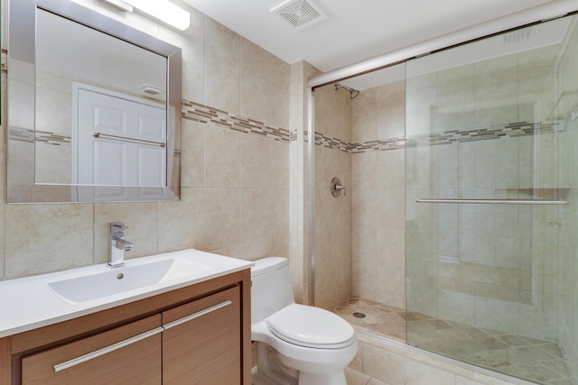 bathroom with toilet, vanity, visible vents, tile walls, and a stall shower