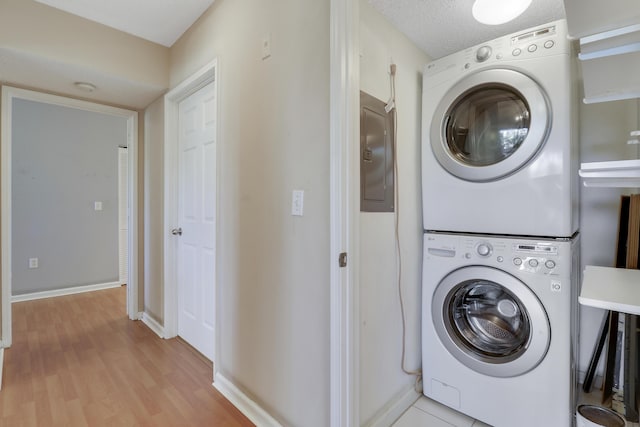 laundry room featuring a textured ceiling, laundry area, light wood-style floors, electric panel, and stacked washer and clothes dryer