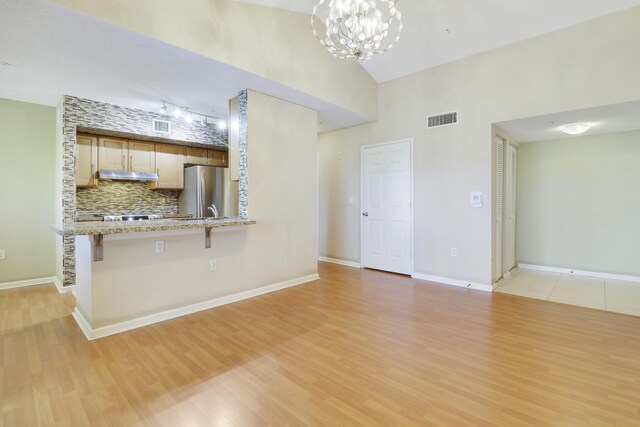 kitchen with visible vents, light wood-style flooring, a breakfast bar, freestanding refrigerator, and under cabinet range hood