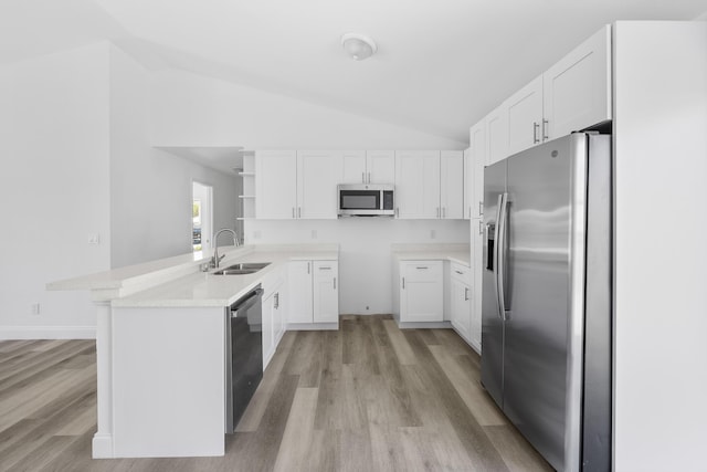 kitchen with appliances with stainless steel finishes, white cabinets, vaulted ceiling, a sink, and a peninsula