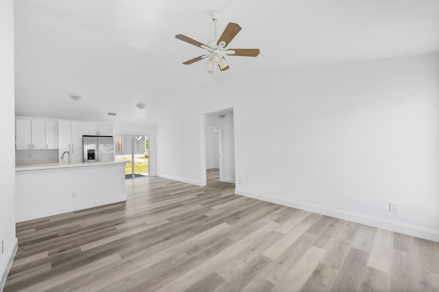 unfurnished living room featuring lofted ceiling, a sink, ceiling fan, light wood-type flooring, and baseboards