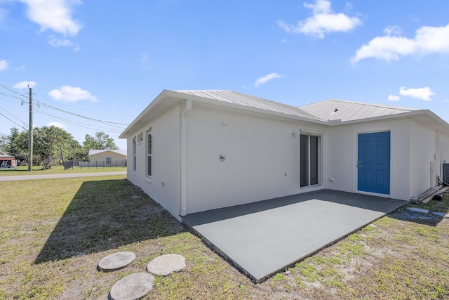 back of property featuring metal roof, a lawn, a patio area, and stucco siding