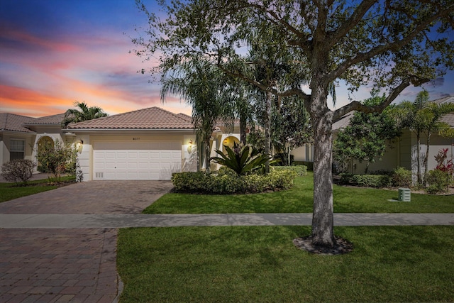 mediterranean / spanish-style house with an attached garage, stucco siding, a front lawn, a tiled roof, and decorative driveway