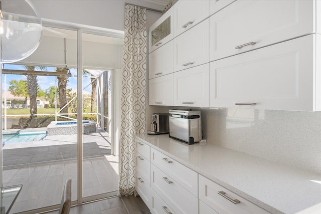 kitchen featuring light stone counters, glass insert cabinets, decorative backsplash, and white cabinetry