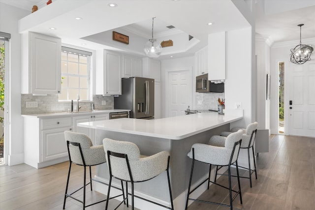 kitchen with crown molding, a tray ceiling, appliances with stainless steel finishes, a peninsula, and a sink