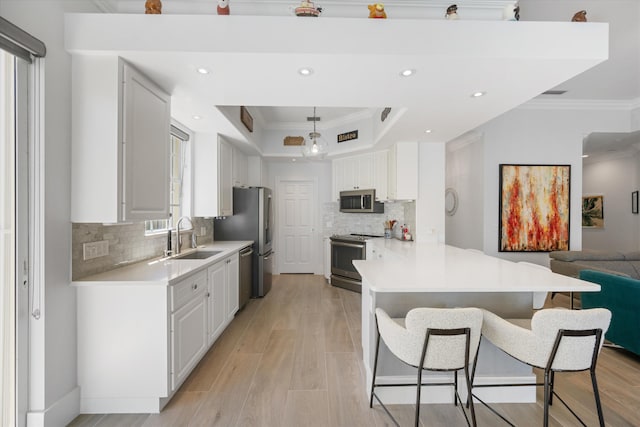 kitchen with a breakfast bar, a sink, white cabinetry, appliances with stainless steel finishes, and crown molding