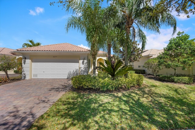 mediterranean / spanish-style home featuring a front yard, an attached garage, stucco siding, a tile roof, and decorative driveway