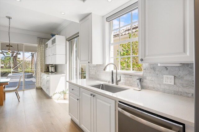 kitchen with ornamental molding, a sink, light countertops, white cabinets, and dishwasher