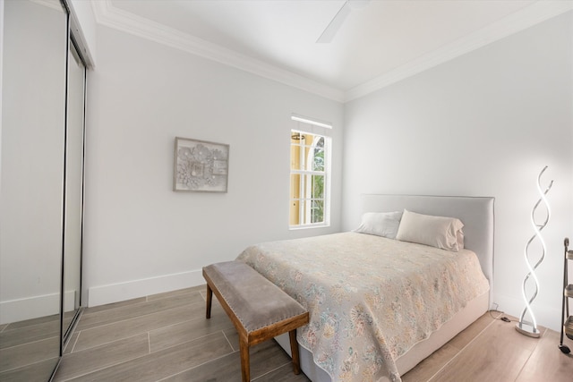 bedroom with a closet, baseboards, wood finished floors, and crown molding