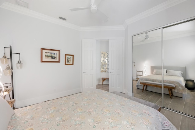 bedroom with visible vents, baseboards, ornamental molding, wood finished floors, and a closet