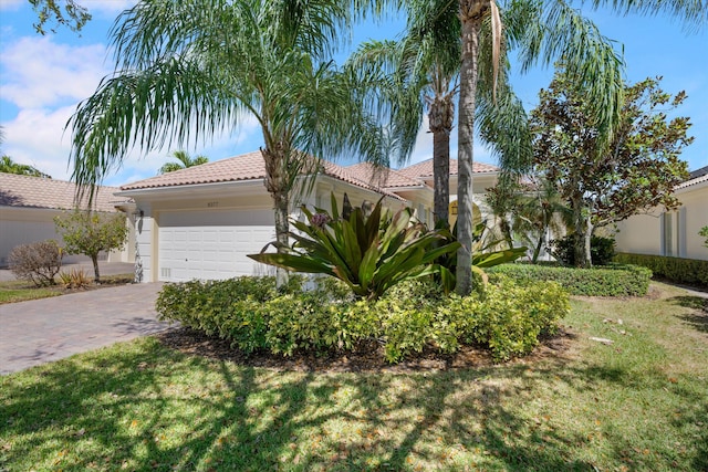 view of front of property with a front yard, an attached garage, stucco siding, a tiled roof, and decorative driveway