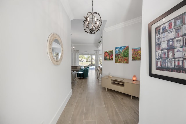 corridor with wood finish floors, baseboards, an inviting chandelier, and ornamental molding