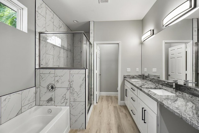 bathroom with wood finished floors, double vanity, a stall shower, a sink, and a garden tub