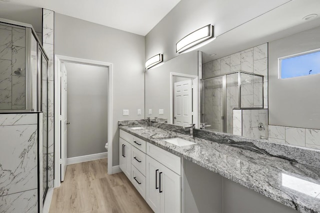 bathroom with a marble finish shower, toilet, double vanity, wood finished floors, and a sink