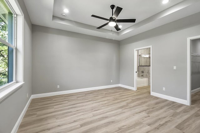 unfurnished bedroom featuring a tray ceiling, light wood-style floors, baseboards, and connected bathroom