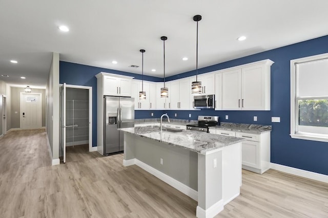 kitchen with light wood-style flooring, a center island with sink, a sink, white cabinetry, and appliances with stainless steel finishes