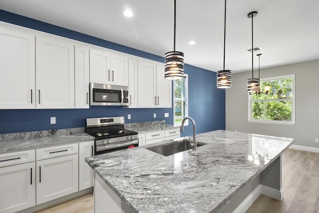 kitchen with white cabinets, stainless steel appliances, an island with sink, and a sink