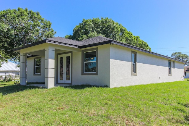 rear view of property featuring french doors, a lawn, and stucco siding