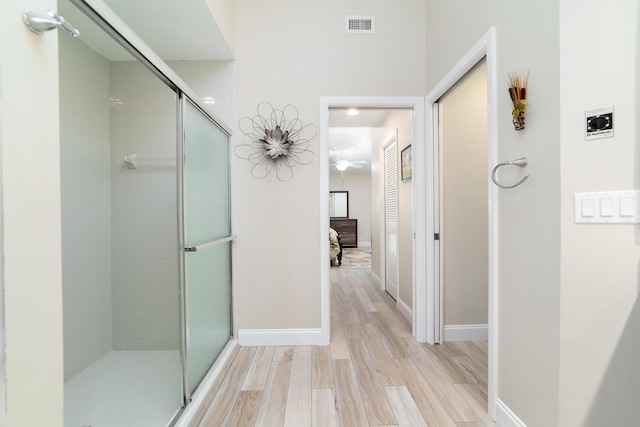 ensuite bathroom with a stall shower, baseboards, visible vents, and wood finished floors