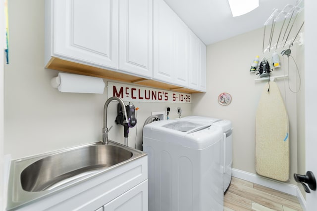 washroom with cabinet space, baseboards, washer and clothes dryer, light wood-type flooring, and a sink