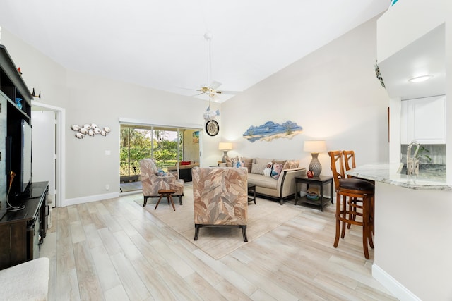 living room featuring baseboards, a high ceiling, a ceiling fan, and light wood-style floors