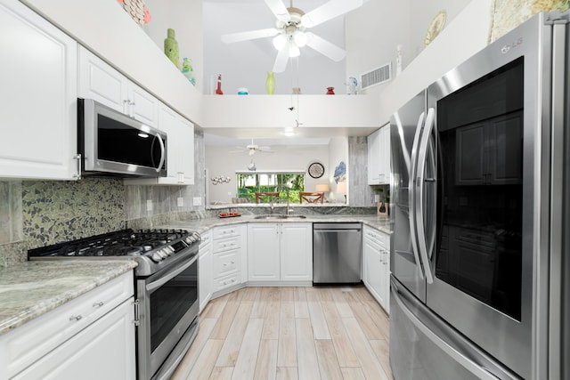 2433 SW Foxpoint Trl, Palm City, FL 34990 - kitchen with stainless steel appliances, ceiling fan, a towering ceiling, white cabinetry, and light stone counters