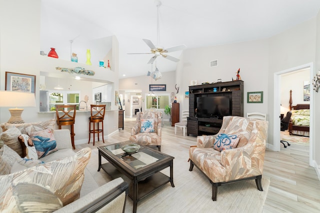 living room with visible vents, baseboards, ceiling fan, light wood-type flooring, and high vaulted ceiling