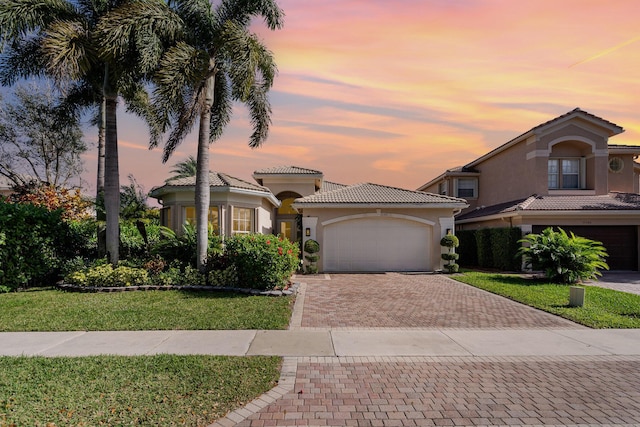 mediterranean / spanish-style house with decorative driveway, stucco siding, an attached garage, a front yard, and a tiled roof