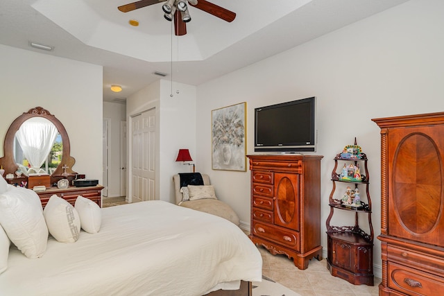 bedroom featuring a tray ceiling, a closet, visible vents, light tile patterned flooring, and ceiling fan