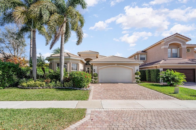 mediterranean / spanish-style house with an attached garage, a tiled roof, decorative driveway, stucco siding, and a front yard