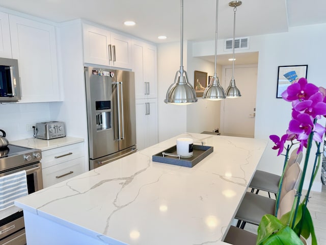 kitchen featuring a breakfast bar area, visible vents, appliances with stainless steel finishes, white cabinets, and light stone countertops