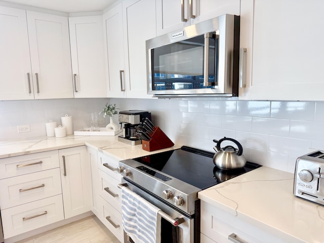 kitchen featuring stainless steel appliances, white cabinets, backsplash, and light stone counters