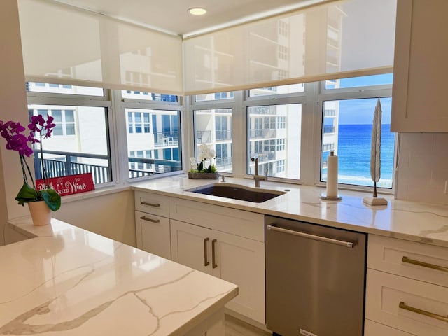 kitchen with stainless steel dishwasher, decorative backsplash, a sink, and light stone countertops