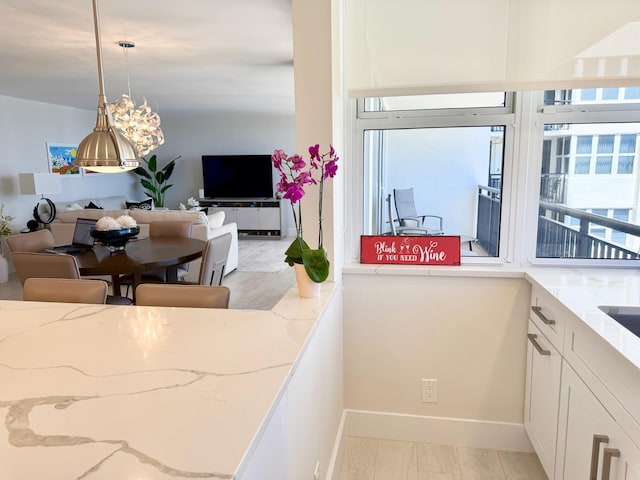 kitchen featuring baseboards, open floor plan, light stone countertops, white cabinetry, and pendant lighting