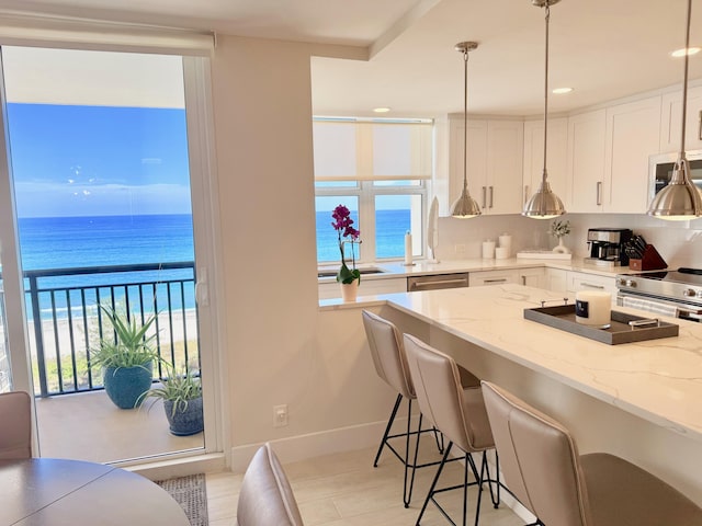 kitchen featuring tasteful backsplash, white cabinets, appliances with stainless steel finishes, light stone counters, and a breakfast bar area