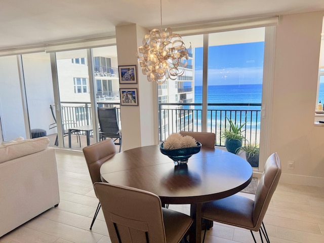 dining area featuring a water view, light wood-style flooring, an inviting chandelier, expansive windows, and baseboards