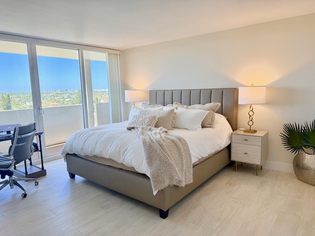 bedroom featuring light wood finished floors, a wall of windows, and baseboards