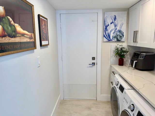 washroom featuring light wood finished floors, washing machine and dryer, cabinet space, and baseboards