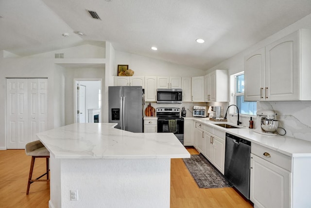 kitchen featuring visible vents, a kitchen island, a kitchen breakfast bar, stainless steel appliances, and a sink