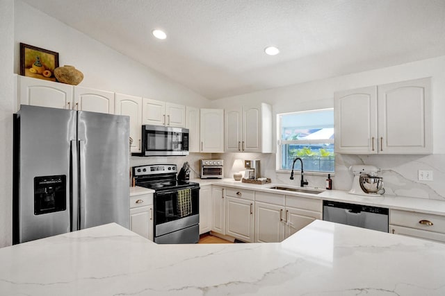 kitchen with light stone counters, a sink, vaulted ceiling, appliances with stainless steel finishes, and tasteful backsplash