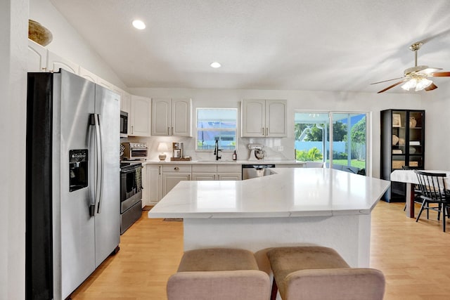 kitchen featuring a kitchen island, light wood-type flooring, decorative backsplash, appliances with stainless steel finishes, and a sink