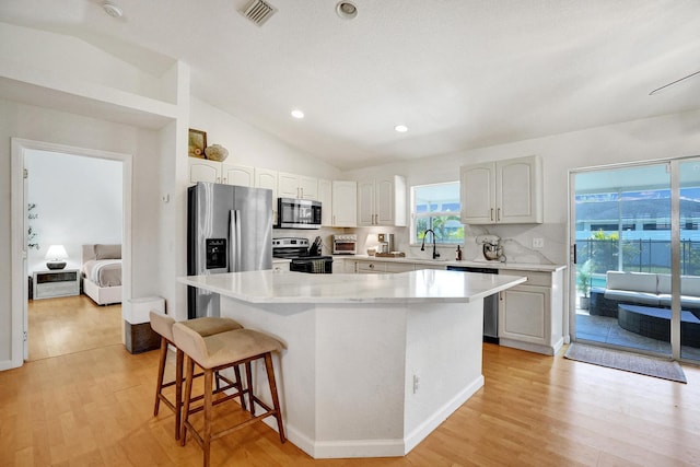 kitchen with light wood-style flooring, a kitchen island, stainless steel appliances, a breakfast bar area, and light countertops